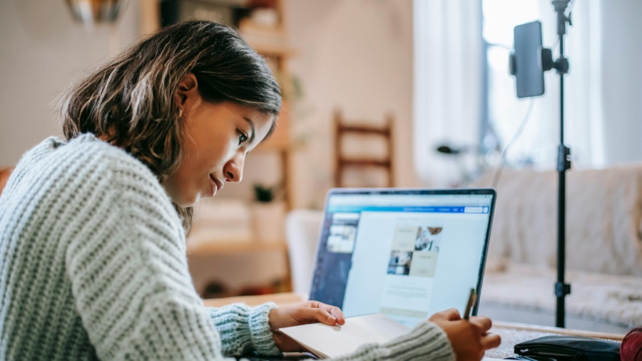 hispanic-lady-studying-on-netbook-while-writing-information-in-notepad